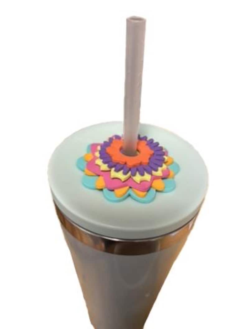 K&ouml;nnte beinhalten: Ein hellgrauer Becher mit einem Blumendesign auf dem Deckel. Der Deckel ist hellgr&uuml;n mit einem bunten Blumendesign in Orange, Lila, Rosa und Blau. Ein grauer Strohhalm ist in den Deckel gesteckt.