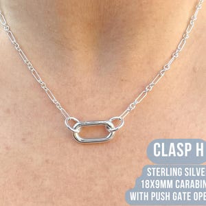 May include: A silver necklace with a carabiner clasp. The necklace features a chain with rectangular links and a central 18x9mm carabiner with a push gate opening. The text "CLASP H" and "STERLING SILVER" are visible.