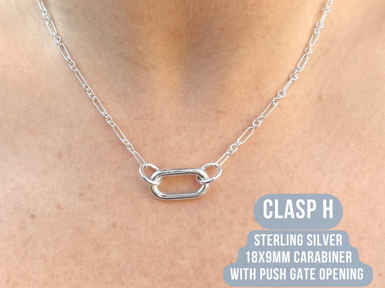 May include: A silver necklace with a carabiner clasp. The necklace features a chain with rectangular links and a central 18x9mm carabiner with a push gate opening. The text "CLASP H" and "STERLING SILVER" are visible.