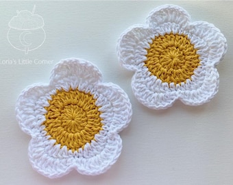 May include: Two crocheted flower coasters with white petals and a yellow center. The coasters are made with a textured stitch.