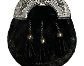 Puede incluir: Un sporran de piel negra con tres borlas negras y una parte superior de metal plateado con un diseño de cardo.