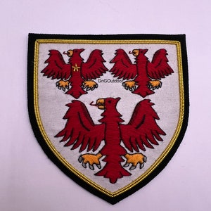 May include: Embroidered patch featuring a white background and three red eagles with gold accents. The patch is bordered in black with a gold trim.