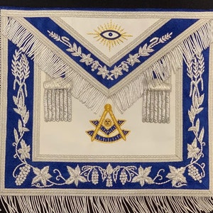 May include: White Masonic apron with blue trim and silver fringe. The apron features an embroidered eye with a sunburst, a compass and square, and a grapevine design.