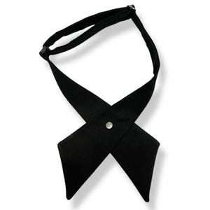 Könnte beinhalten: Eine schwarze Krawatte aus Stoff mit einem einzigen silbernen Knopf in der Mitte. Die Krawatte ist so konzipiert, dass sie am Hals gekreuzt getragen wird.