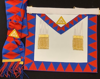 Puede incluir: Un delantal masónico blanco con un borde rojo y azul. El delantal tiene dos cintas blancas con borlas doradas. El delantal tiene un triángulo dorado con la letra 'G' en el centro.