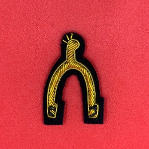 May include: A gold embroidered horseshoe-shaped patch with a black felt backing. The horseshoe is outlined in black thread and has a small gold loop at the top.
