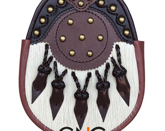 Può includere: Uno sporran in pelle bianca e marrone con una frangia e una fibbia in ottone decorativa. Lo sporran ha una patta in pelle marrone con un cerchio di borchie in ottone.