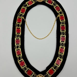 May include: A gold chain with red enamel squares and a gold star pendant. The chain is on a black velvet background.