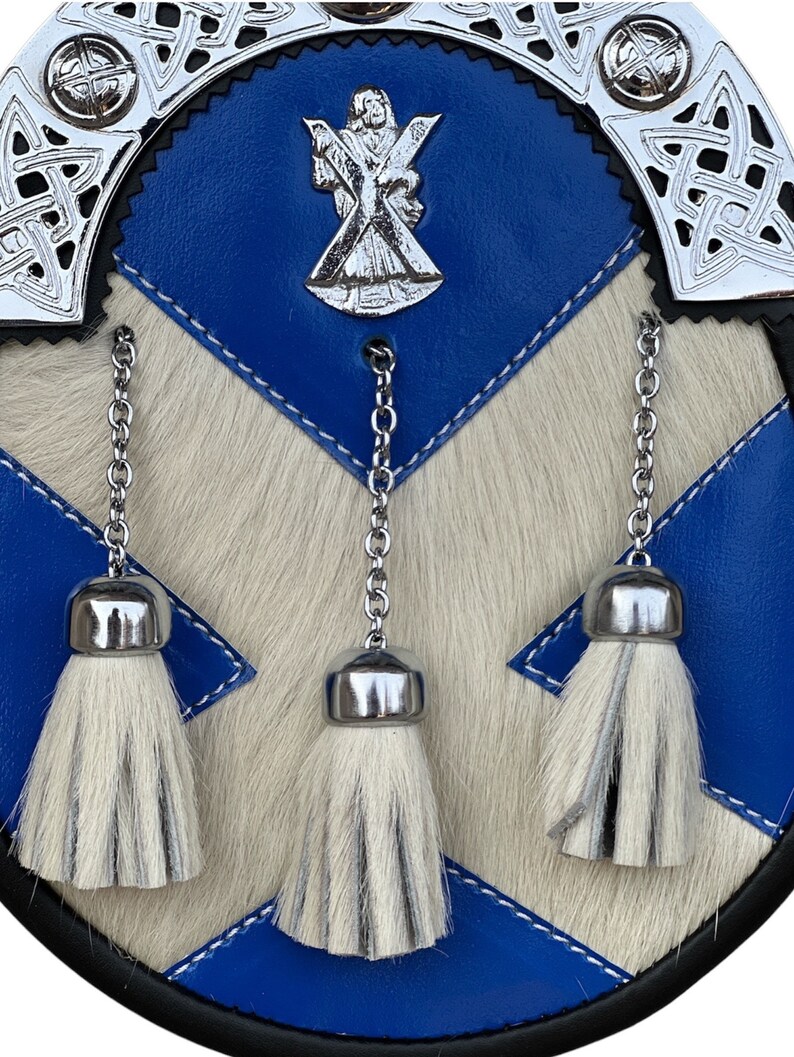 May include: A blue and white kilt sporran with three white tassels and a silver metal embellishment featuring a cross and a figure.
