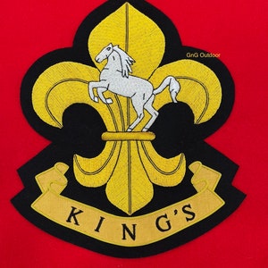 May include: A black embroidered patch with a gold fleur-de-lis and a white horse. The patch has a gold ribbon with the text "KING'S" on it.