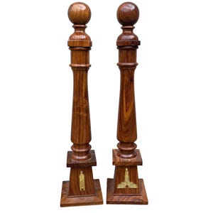 May include: Two wooden decorative pillars with a rounded top and a square base. Each pillar has a gold emblem on the front of the base.