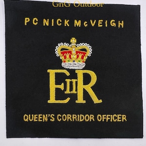 May include: A black embroidered patch with gold thread depicting the royal cypher "ER" with a crown above and the text "PC NICK McVEIGH QUEEN'S CORRIDOR OFFICER".