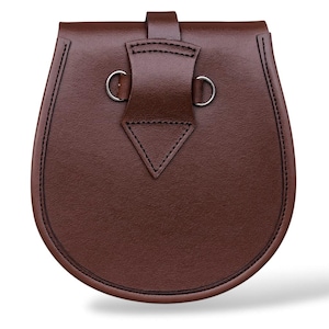 May include: A brown leather sporran with a rounded bottom and a flap closure. The sporran has a decorative stitched border and silver-colored metal rings. The flap is secured with a leather strap.