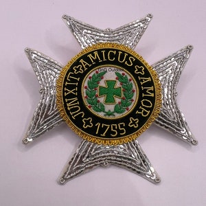 May include: A silver and gold embroidered badge with a black circle in the centre. The circle has the text "AMICUS & AMOR" and "1755" around a green wreath with a red cross in the centre.