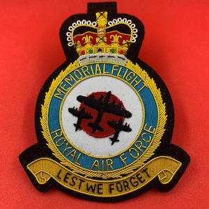 May include: A black and gold embroidered patch with a crown, a circle with the words "Memorial Flight Royal Air Force" and a red circle with three black airplanes, and a gold banner with the words "Lest We Forget".