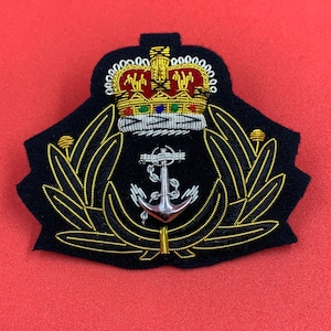 May include: A black embroidered patch with a gold crown, anchor, and laurel wreath. The crown has red and green jewels.