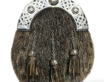 Può includere: Uno sporran in pelliccia marrone con catena e nappe argentate. Lo sporran ha un design a nodo celtico argentato nella parte superiore.
