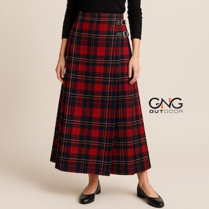 May include: A long, red and black plaid wrap skirt featuring two black leather side straps with silver-toned metal buckles at the waist. The skirt has a straight silhouette and is paired with a black long-sleeved top. The GNG OUTDOOR logo is visible.