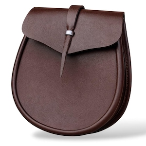 May include: A brown leather sporran with a curved bottom and a flap closure. The flap is secured with a leather strap and a silver-colored metal ring. The sporran is a traditional Scottish accessory.