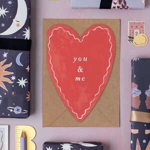 a large red heart-shaped card with the text "you & me" written on it, surrounded by various other items such as a ruler, a star, and a stamp.