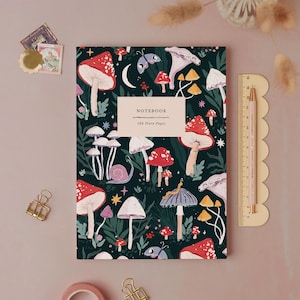 Puede incluir: Un cuaderno rectangular con cubierta verde oscuro que presenta un patrón de setas rojas, blancas y moradas, caracoles y mariposas. Una etiqueta central dice NOTEBOOK 192 Plain Pages. Una regla muestra una altura de 20 cm.