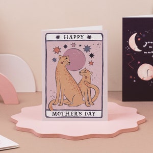 Mothers Day card with tarot card style artwork of leopard mum and little leopard in the style of a tarot card with a pink background and stars.