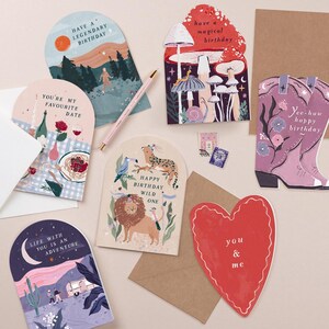 a variety of birthday cards and stationery items, including a red heart-shaped card, a pink envelope, and several other cards with different designs and messages.