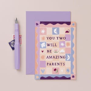 Puede incluir: Una tarjeta de felicitación con un patrón de cuadros en tonos melocotón, lavanda y azul, con el texto YOU TWO WILL BE AMAZING PARENTS, rodeado de iconos de estrellas, lunas, flores y una mariquita, acompañada de un sobre y bolígrafo lavanda.