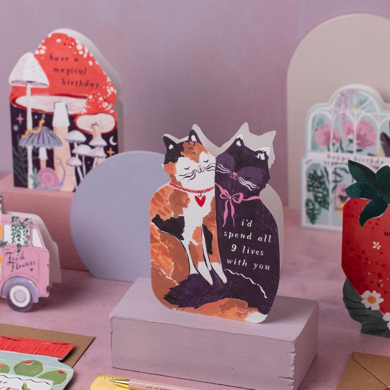 The perfect anniversary card or Valentines card for a cat lover, this uniquely shaped greeting card is cut into the shape of two snuggling cats. The adorable cat cards are blank on the inside, ready for a handwritten romantic message to be added