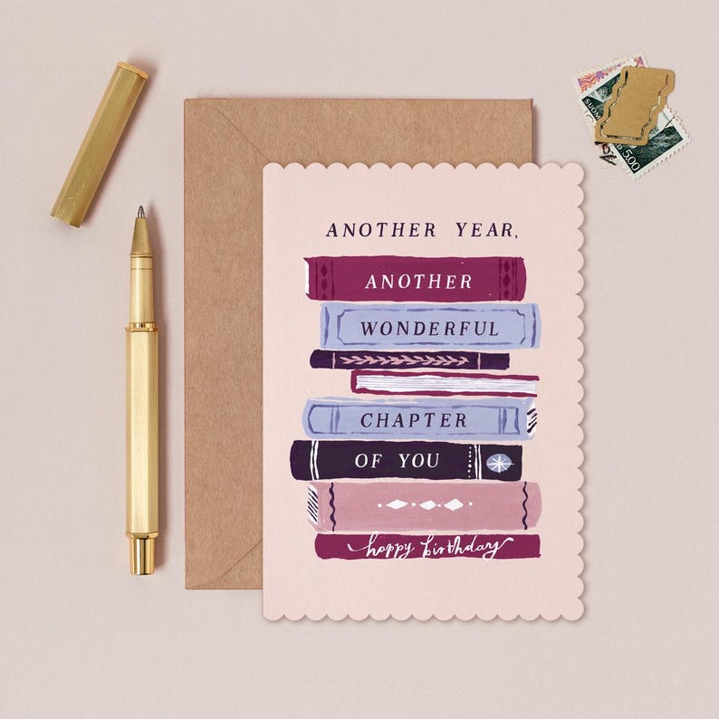 a birthday card with a scalloped edge, a stack of books, a pen, and some postage stamps.