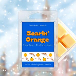 May include: A clear plastic clamshell package containing orange-colored wax melts. The label reads "Soarin' Orange" with the text "Orange Blossom + Citrus Groves + Sunshine." The product is from Yellow Flame Candle Co.
