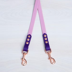 May include: A pink and purple dog lead with two rose gold clips and four rose gold accents.