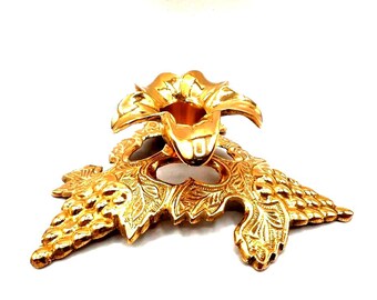 May include: Ornate gold-colored candle holder with a floral design. The base features detailed grape leaf and vine motifs. The candle holder is made of metal and has a glossy finish. The overall design is elegant and decorative.