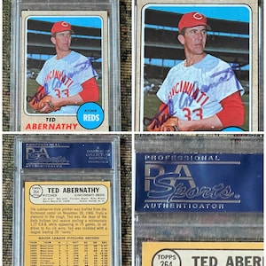 Puede incluir: Una tarjeta de béisbol Topps de 1968 con Ted Abernathy, un lanzador de los Cincinnati Reds. La tarjeta está calificada PSA EX 5 y tiene un número de certificación PSA/DNA de 16797704. La tarjeta muestra a Abernathy con su uniforme de los Reds, sosteniendo un guante de béisbol y usando una gorra roja con una 'C' blanca. La tarjeta también incluye la firma de Abernathy.