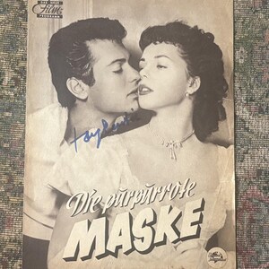 May include: Vintage black and white movie poster for "Die purpurrote Maske" featuring a man and woman in a romantic embrace. The poster includes the film title, a logo, and an autograph in blue ink.