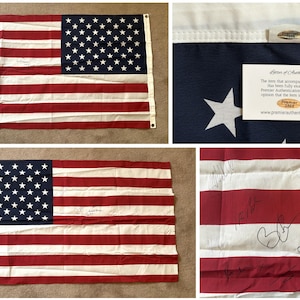 May include: An American flag with red and white stripes and a blue canton filled with white stars. The flag has signatures on it and a Premier Authentication card.