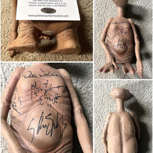 May include: A collection of images featuring an E.T. the Extra-Terrestrial figure. The figure is tan with blue eyes and has multiple signatures on its chest. A Premier Authentication letter is also included.