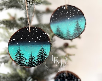 Peut inclure: Trois ornements ronds en tranches de bois peints avec une scène d'hiver. Les ornements présentent un ciel bleu foncé avec des étoiles blanches, une forêt vert turquoise et des arbres noirs.