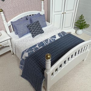 Könnte beinhalten: Ein weißes Holzbettgestell mit einer blauen und weißen gemusterten Bettdecke und einer blauen Tagesdecke. Das Bett hat ein Kopfteil mit einer abgerundeten Oberseite und dekorativen Spindeln. Auf dem Bett liegen drei Kissen, zwei gestreift und eines gemustert.