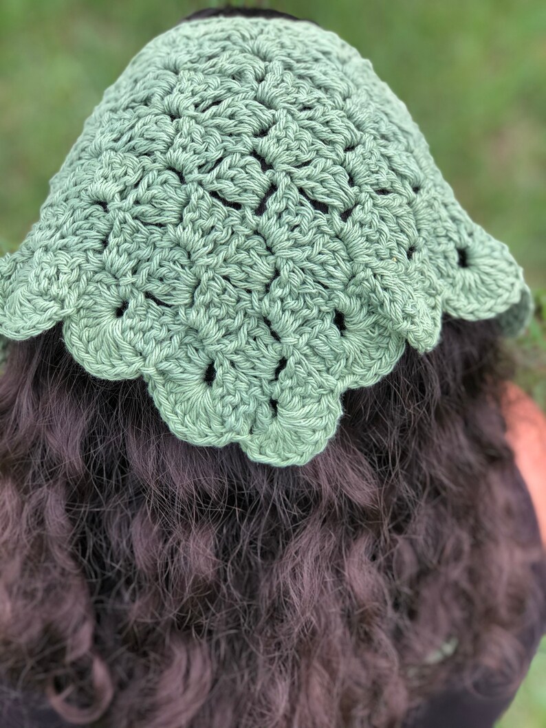 Puede incluir: Un sombrero de ganchillo verde salvia con un borde festoneado. El sombrero est&aacute; hecho de un hilo texturizado y tiene un dise&ntilde;o calado detallado. El sombrero se muestra desde atr&aacute;s, con cabello oscuro visible debajo.