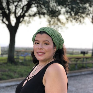 Puede incluir: Un cubrecabezas verde tejido a ganchillo. El cubrecabezas est&aacute; hecho de hilo verde claro y tiene un dise&ntilde;o abierto y calado. La persona lleva una camiseta negra y un collar.