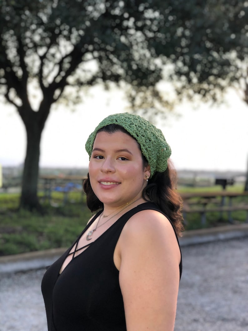 Puede incluir: Un cubrecabezas verde tejido a ganchillo. El cubrecabezas est&aacute; hecho de hilo verde claro y tiene un dise&ntilde;o abierto y calado. La persona lleva una camiseta negra y un collar.