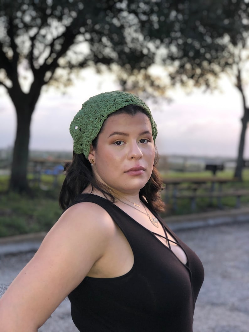 Puede incluir: Se lleva una diadema verde de ganchillo. La diadema est&aacute; hecha de un hilo texturizado y tiene un tejido ligeramente abierto. La persona lleva una camiseta sin mangas negra y un collar. El fondo est&aacute; borroso con &aacute;rboles y un cielo crepuscular.