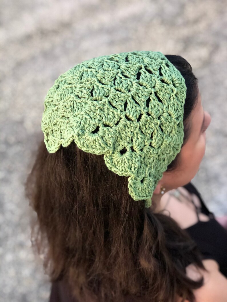 Puede incluir: Una diadema de ganchillo verde claro con un borde festoneado. La diadema est&aacute; hecha de un hilo texturizado y se usa en la cabeza. La imagen es un primer plano de la diadema y la parte posterior de la cabeza de una persona.