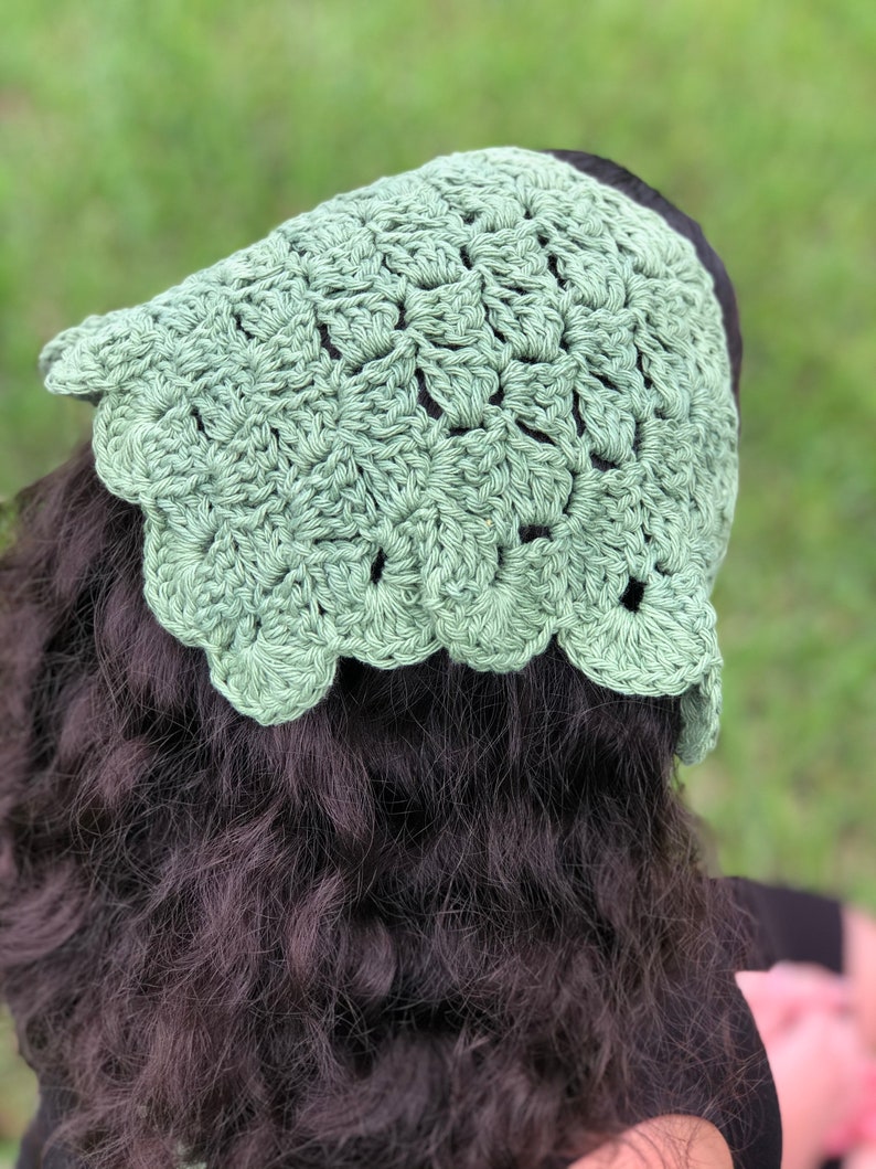 Puede incluir: Un gorro de ganchillo verde claro con un borde festoneado. El tocado hecho a mano est&aacute; hecho de un hilo texturizado y se muestra desde atr&aacute;s, con cabello oscuro visible debajo de la gorra. El gorro es de un color verde suave y apagado.
