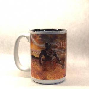 May include: White ceramic mug with a black rim and handle. The mug features a colorful image of a warrior with a weapon, standing in a fiery landscape. The text "SHAMAN" is visible on the mug.