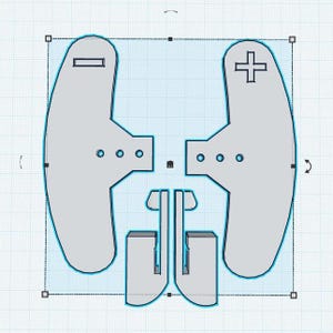 May include: A top-down view of a gray, symmetrical, 3D-printed object. The design features two curved, paddle-like shapes, each with a distinct symbol: a minus sign and a plus sign. The design also includes a central connecting piece and two rectangular elements.