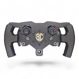 May include: A carbon fiber steering wheel with integrated gaming controls. The wheel features a central emblem and colored buttons. The design includes a directional pad and a series of buttons, with a textured grip on the handles.