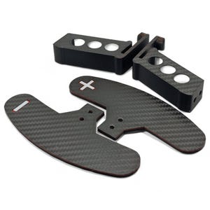 May include: A set of black carbon fiber paddle shifters and mounting brackets. The paddle shifters have a curved design with a red border and a white cross marking. The brackets have three circular holes.