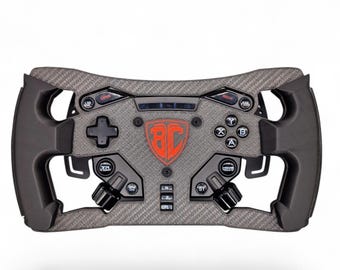 May include: A racing steering wheel controller featuring a dark gray carbon fiber texture, black ergonomic side grips, and a central red shield logo with the letters BC. It includes various buttons labeled DAS, BOX, TR, HOME, N, P, PL, and standard game controller buttons.